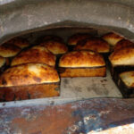 Kırmızı tuğla ve metal çatılı, tekerlekli ayaklar üzerinde duran, barbekü eklentisi olan seyyar taş fırın modeli.