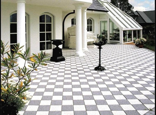 Beyaz kolonlu bir villa girişinde siyah ve beyaz renklerin kontrastıyla oluşturulmuş estetik beton parke taşı kaplaması. Bahçe teras alanında dama desenli siyah beyaz mineral yüzeyli beton parke taşı uygulaması.