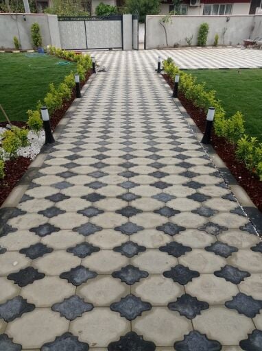 Yanları peyzaj düzenlemesi ve bahçe aydınlatmaları ile çevrelenmiş, elips desenli simetrik parke taşı döşemesi örneği. Bahçe yürüyüş yolunda uygulanmış elips desenli antrasit ve gri dekoratif beton parke taşı.
